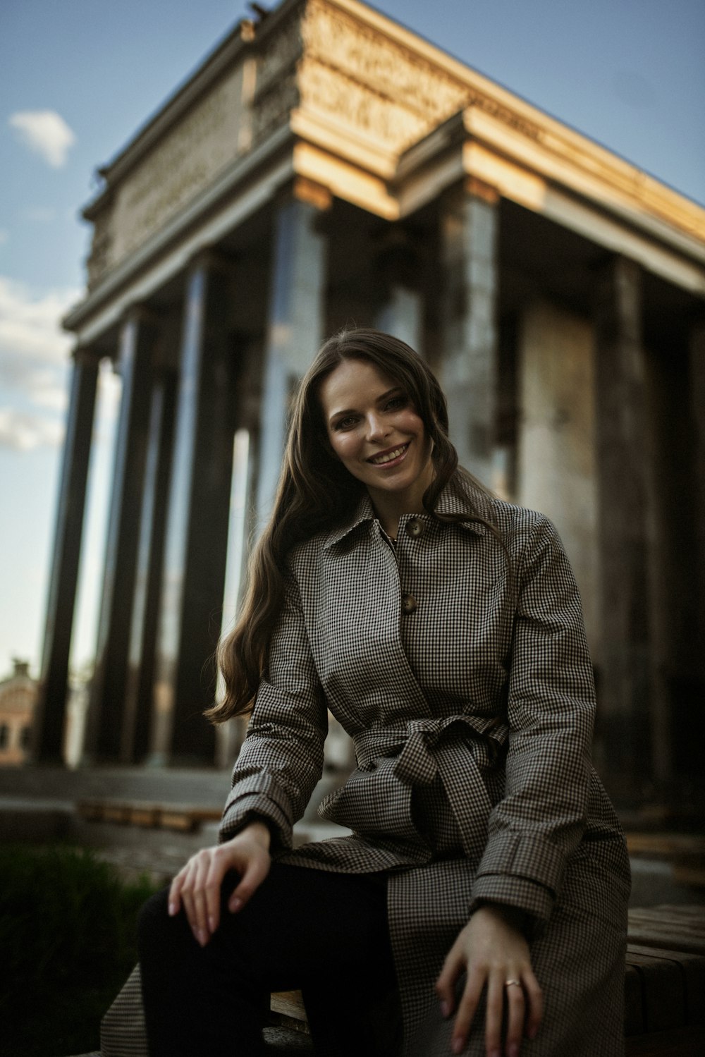 woman in gray and black striped coat sitting on brown wooden bench during daytime