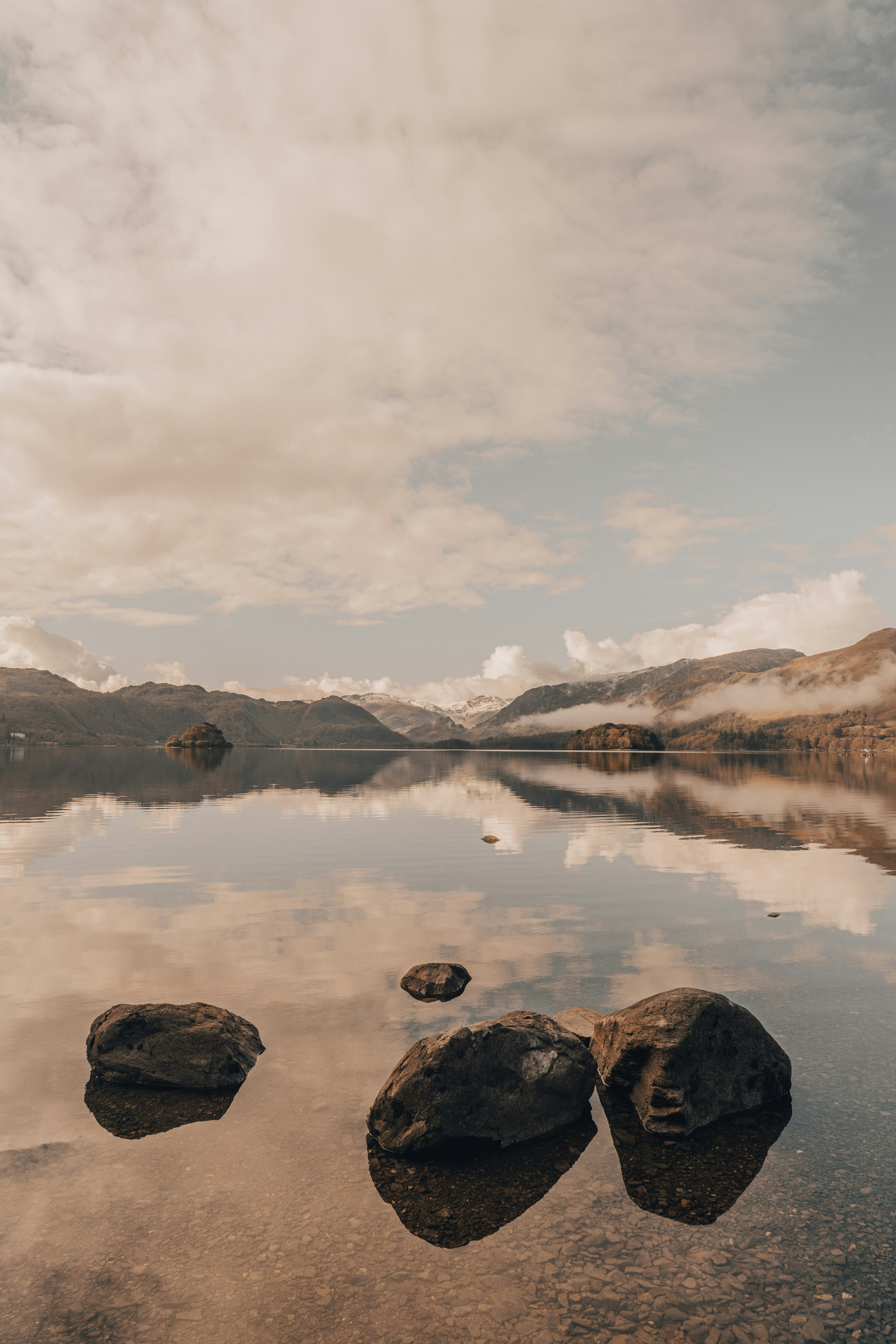 brown and white mountains beside lake under white clouds during daytime