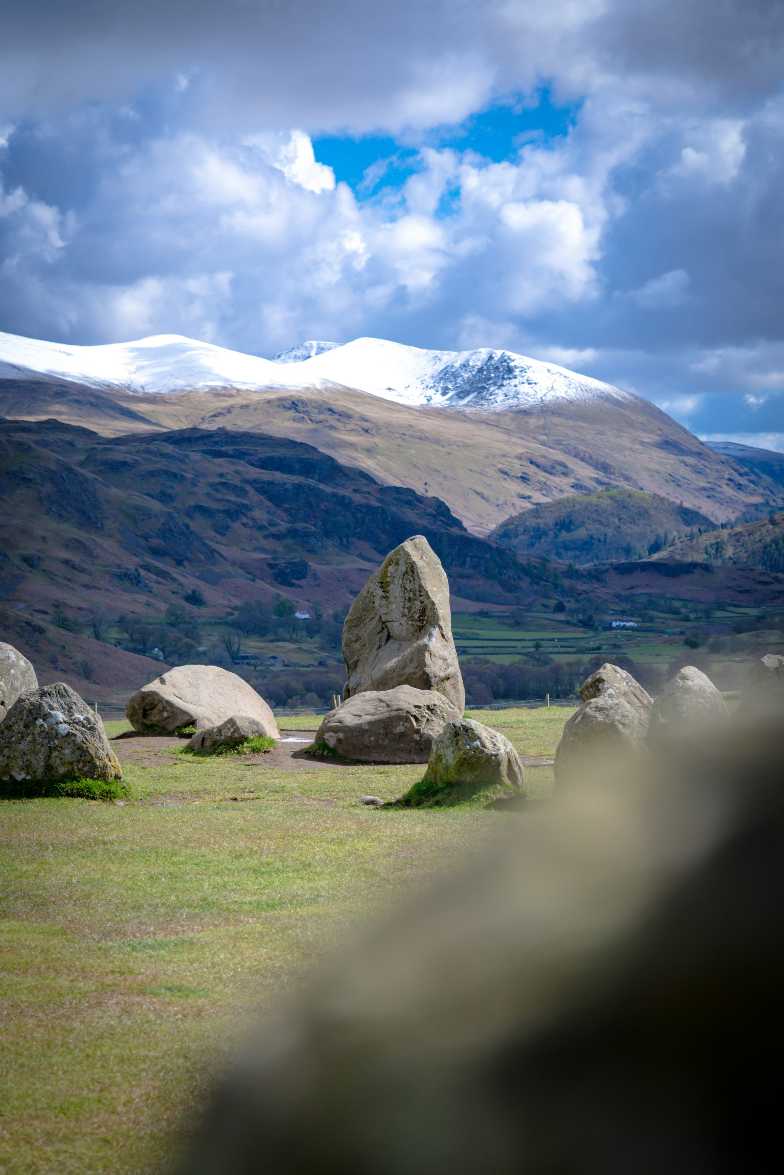 gray rocks on green grass field near brown mountain under white clouds during daytime