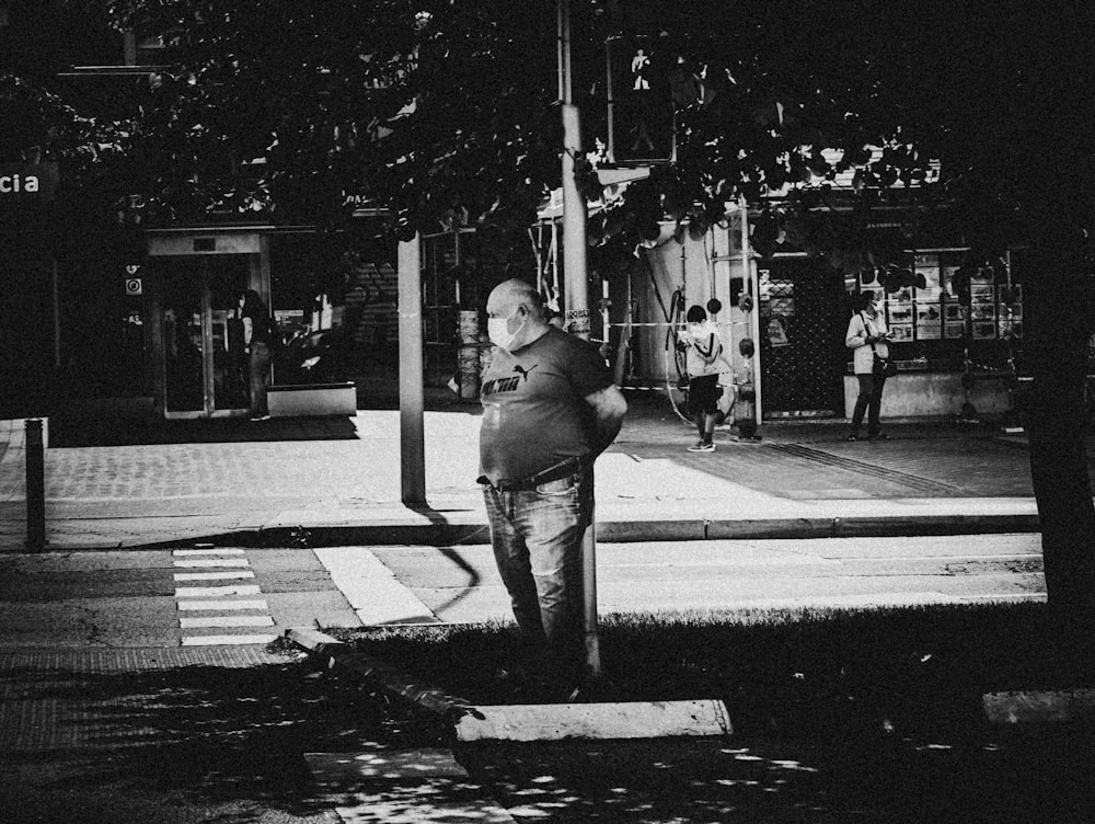 man in black jacket and pants standing on pedestrian lane in grayscale photography