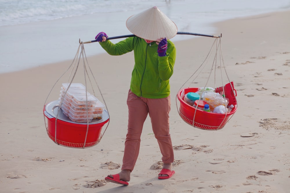 a woman carrying two baskets of food on a beach