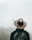 A person wearing a cowboy hat and a backpack faces away, looking at a distant, fog-shrouded temple. The scene is misty, creating an ethereal atmosphere.