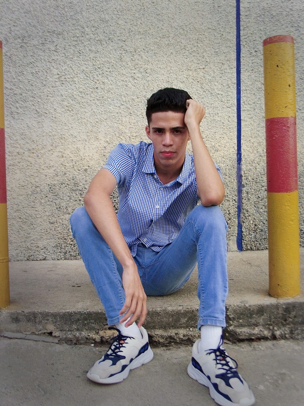 Mann in blau-weiß kariertem Button-Up-Shirt und blauer Jeans auf Beton sitzend