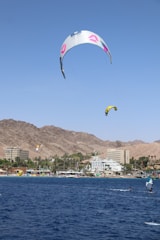 Coach and student smiling on their boards at El Médano, kite soaring in a clear blue sky.