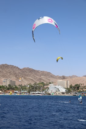Coach and student smiling on their boards at El Médano, kite soaring in a clear blue sky.