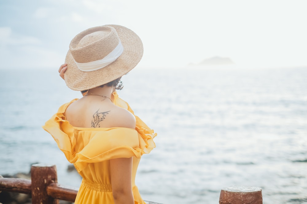 woman in yellow dress wearing white sun hat standing on brown wooden dock during daytime