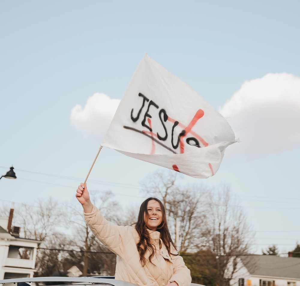 woman in beige long sleeve shirt holding white and red banner