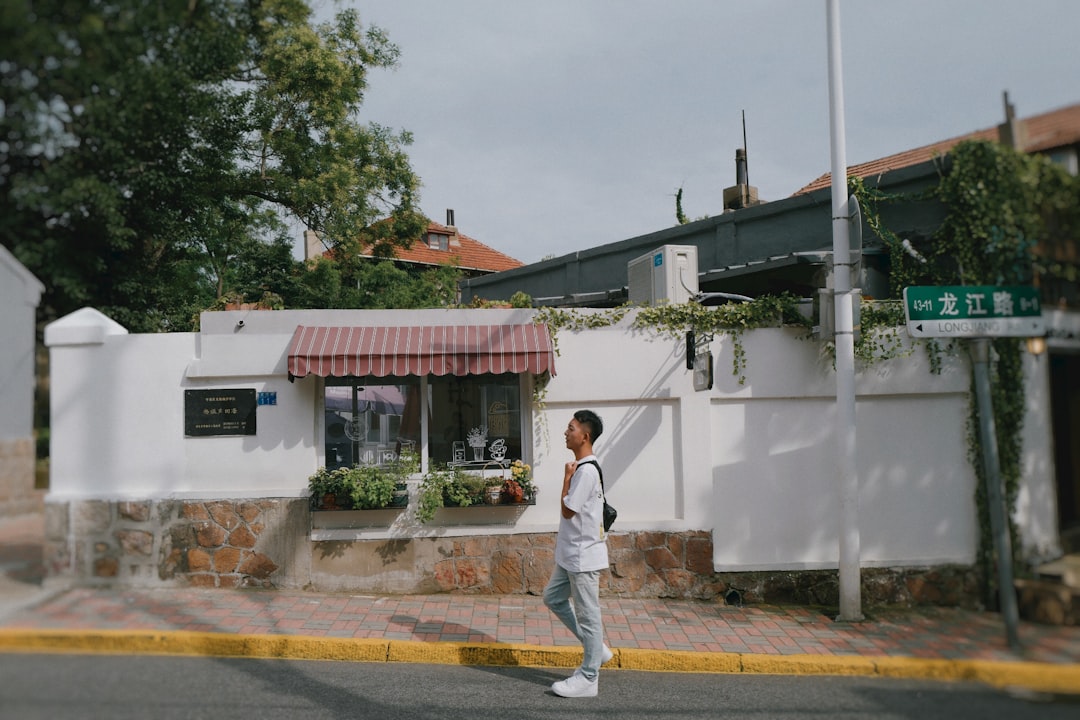 man in white t-shirt and brown pants standing on sidewalk during daytime