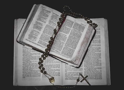 A stack of open books with a cross pendant resting on top.
