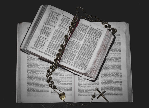 A peaceful study desk with opened theology books and a rosary on top.