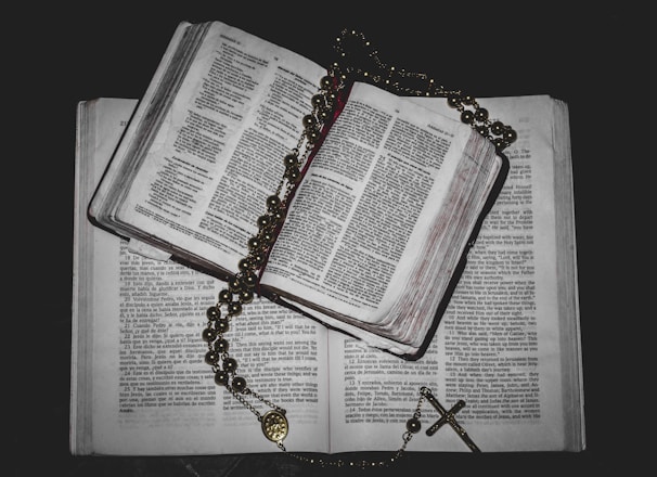 Stack of books by Rafael de San Juan displayed on a wooden table with a rosary beside them.