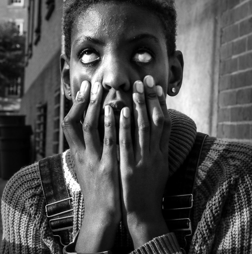 grayscale photo of man in sweater covering his face