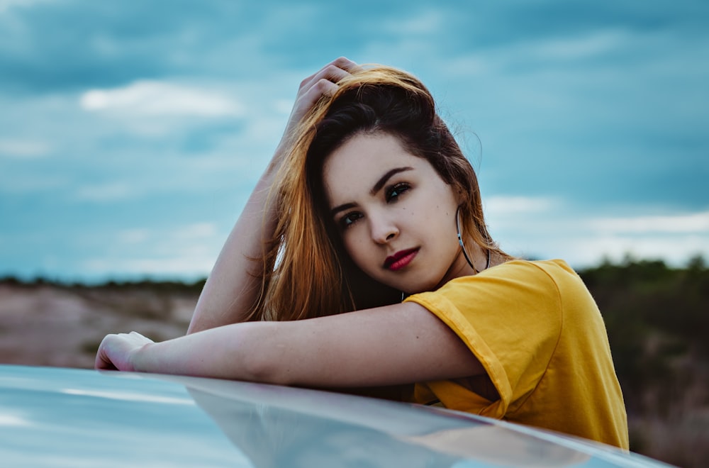 woman in yellow shirt lying on blue and white surfboard during daytime