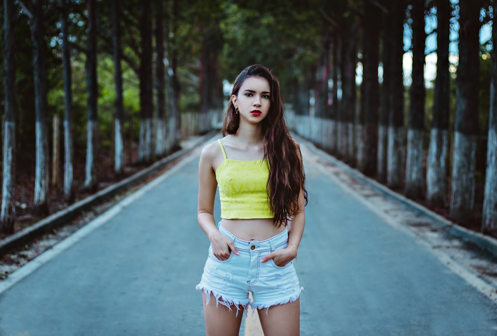 woman in yellow tank top and blue denim shorts standing on pathway during daytime