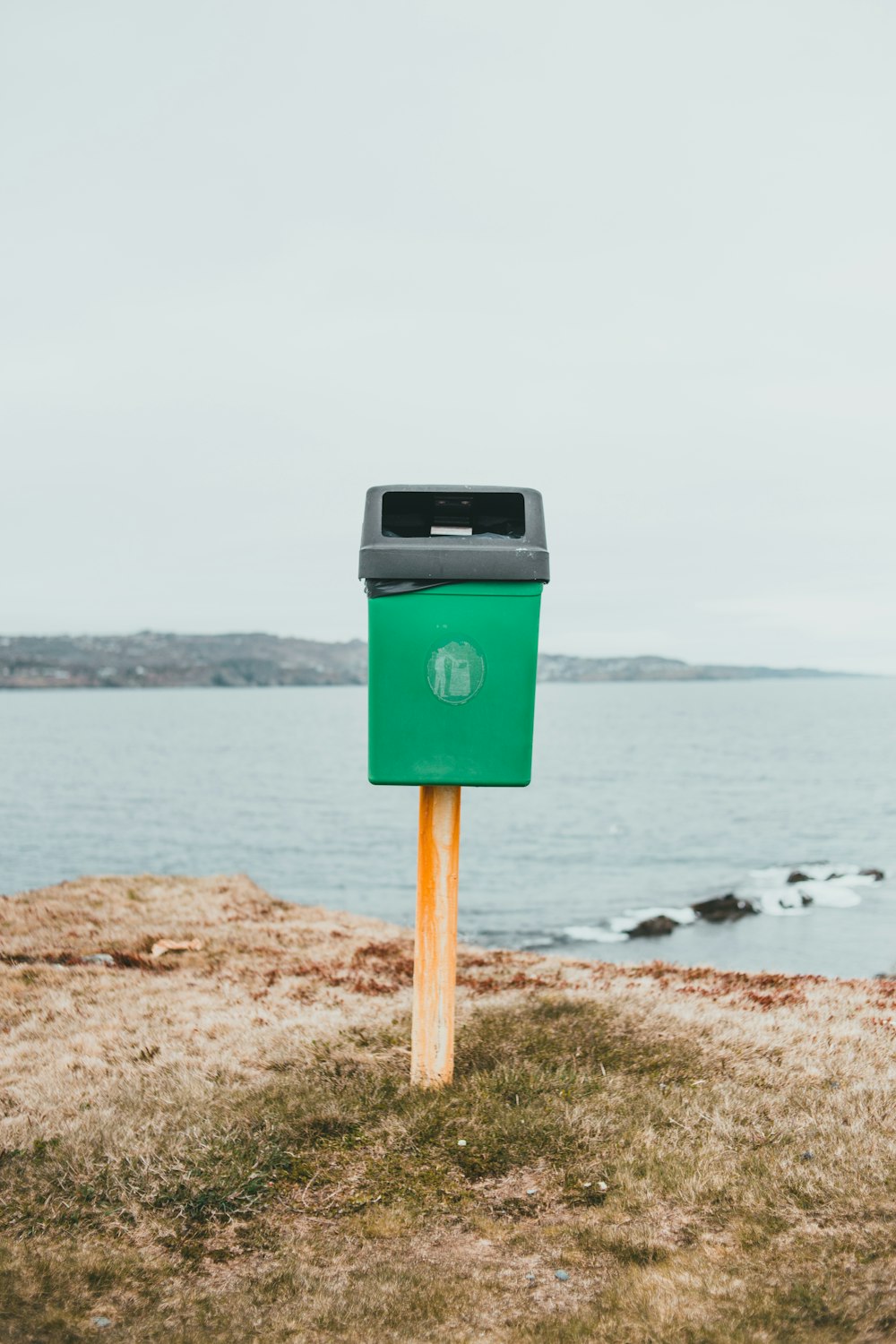 blue and black trash bin on brown sand near sea during daytime