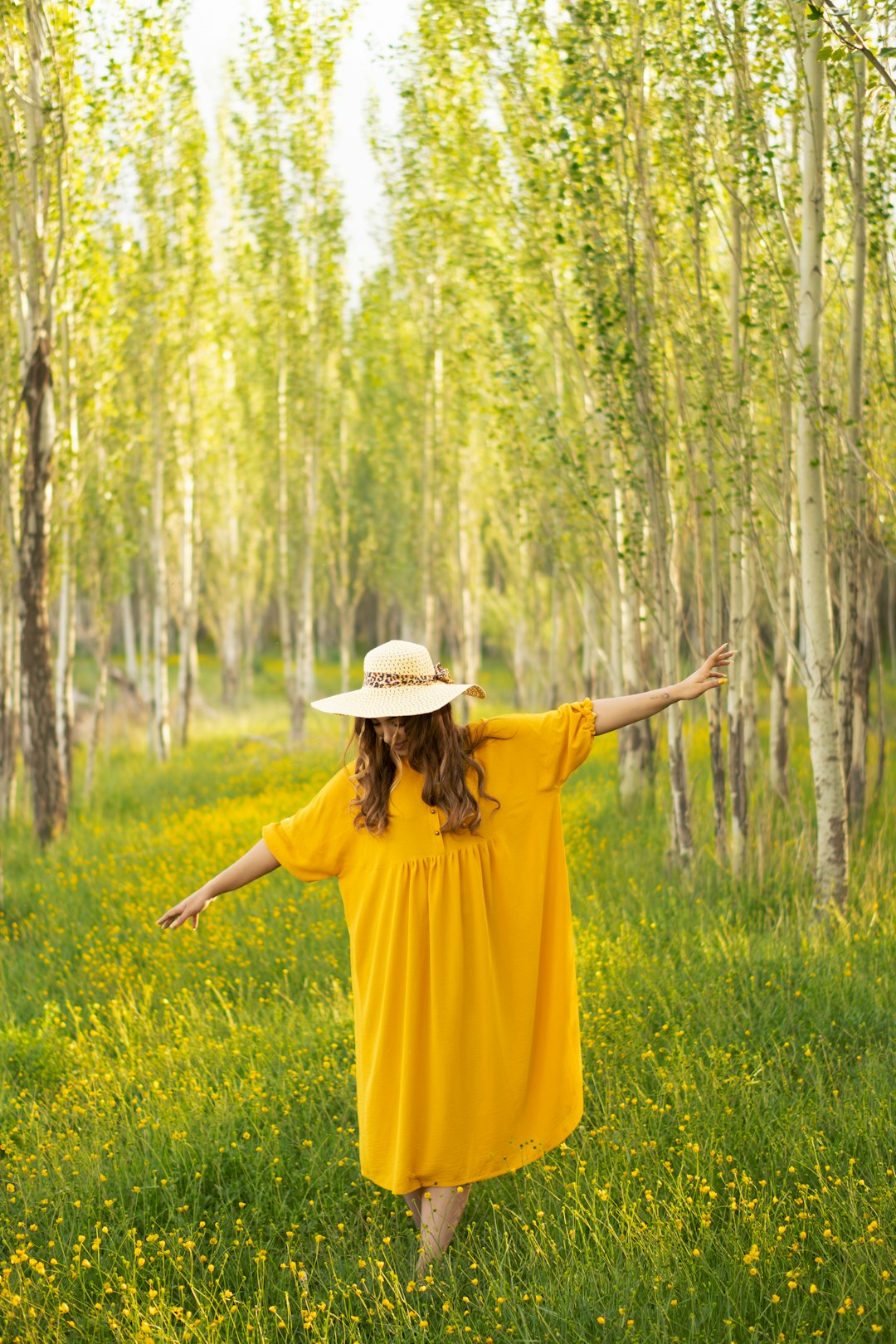 woman in yellow dress wearing brown hat standing on green grass field during daytime
