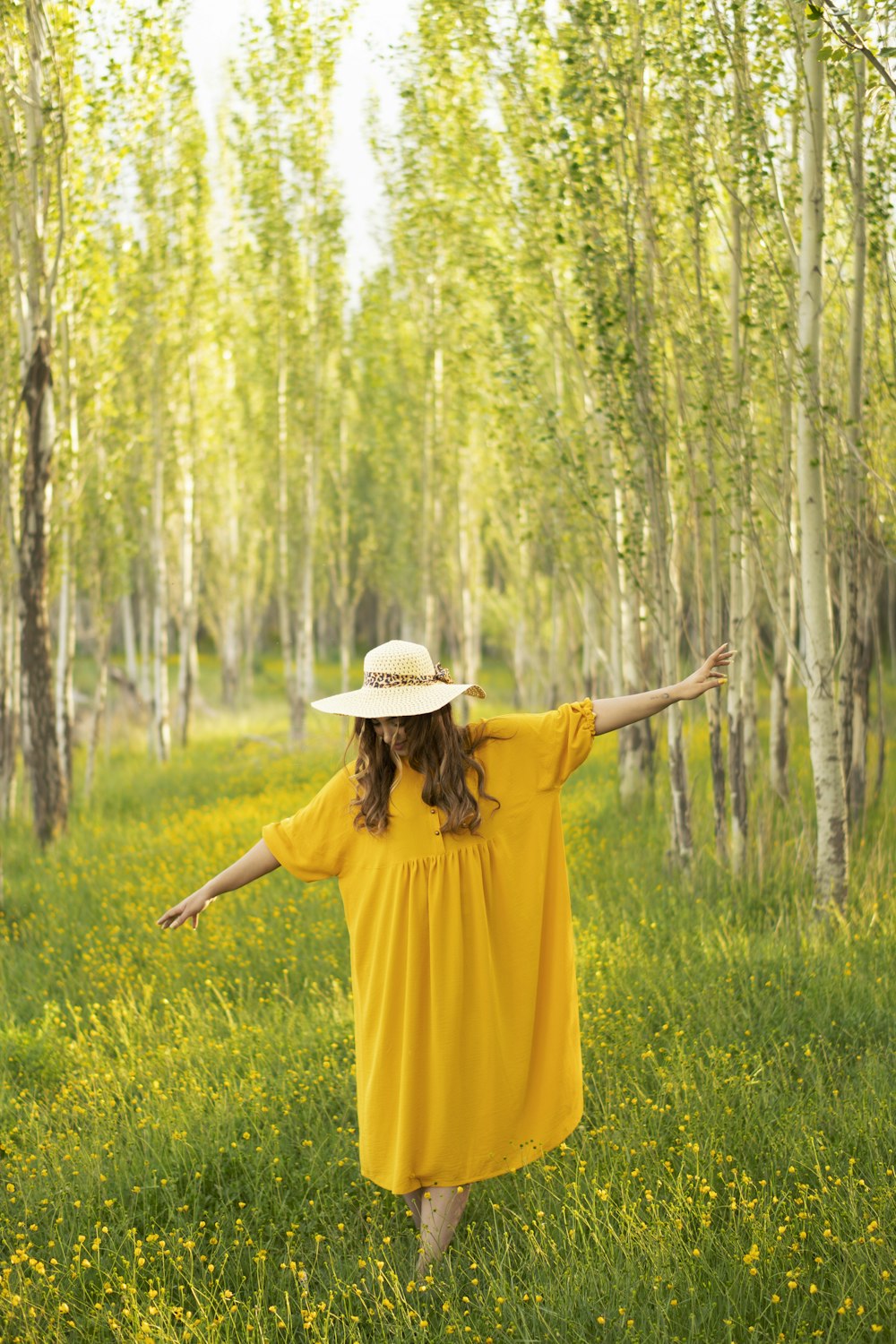 茶色の帽子をかぶった黄色いドレスを着た女性が昼間、緑の芝生の上に立っている