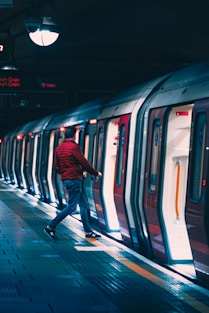 man in black jacket and blue denim jeans standing beside white and blue train
