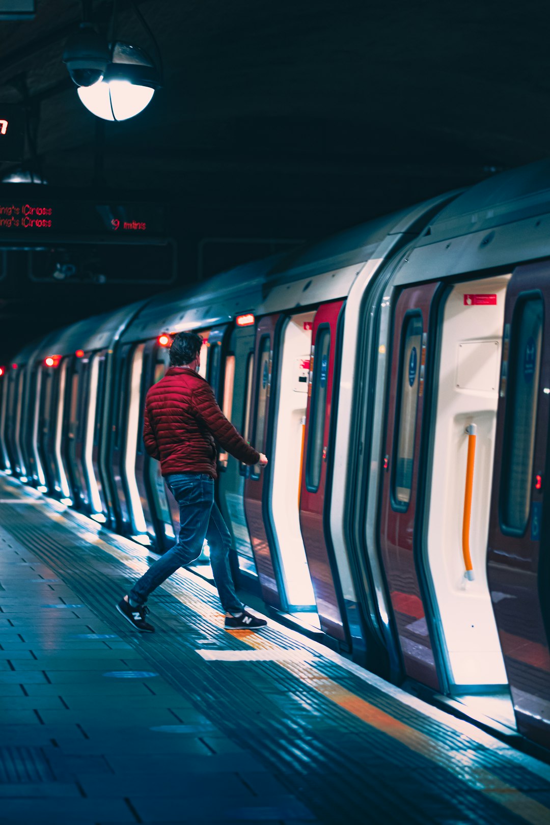 man in black jacket and blue denim jeans standing beside white and blue train