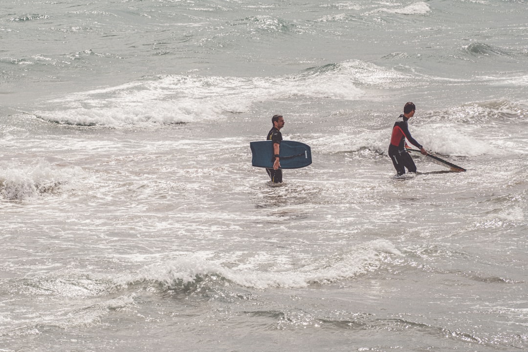 man in black and red wet suit carrying blue surfboard on sea waves during daytime