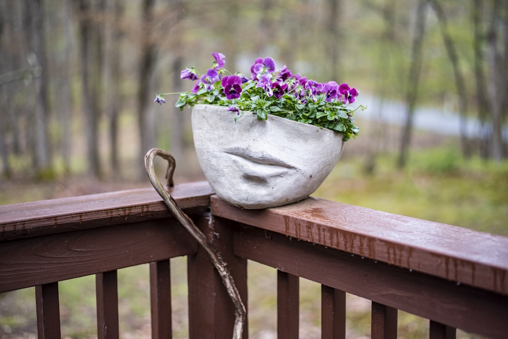 purple flowers in white ceramic vase on brown wooden fence