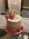 A beautifully decorated birthday cake with a smooth white frosting wave pattern. The cake is adorned with elegant pink roses and a clear balloon, along with a decorative sign that reads 'Happy Birthday'. Gold beads are scattered on the cake, adding a touch of luxury. The cake sits on a pink textured base, with a delicate lace tablecloth underneath.
