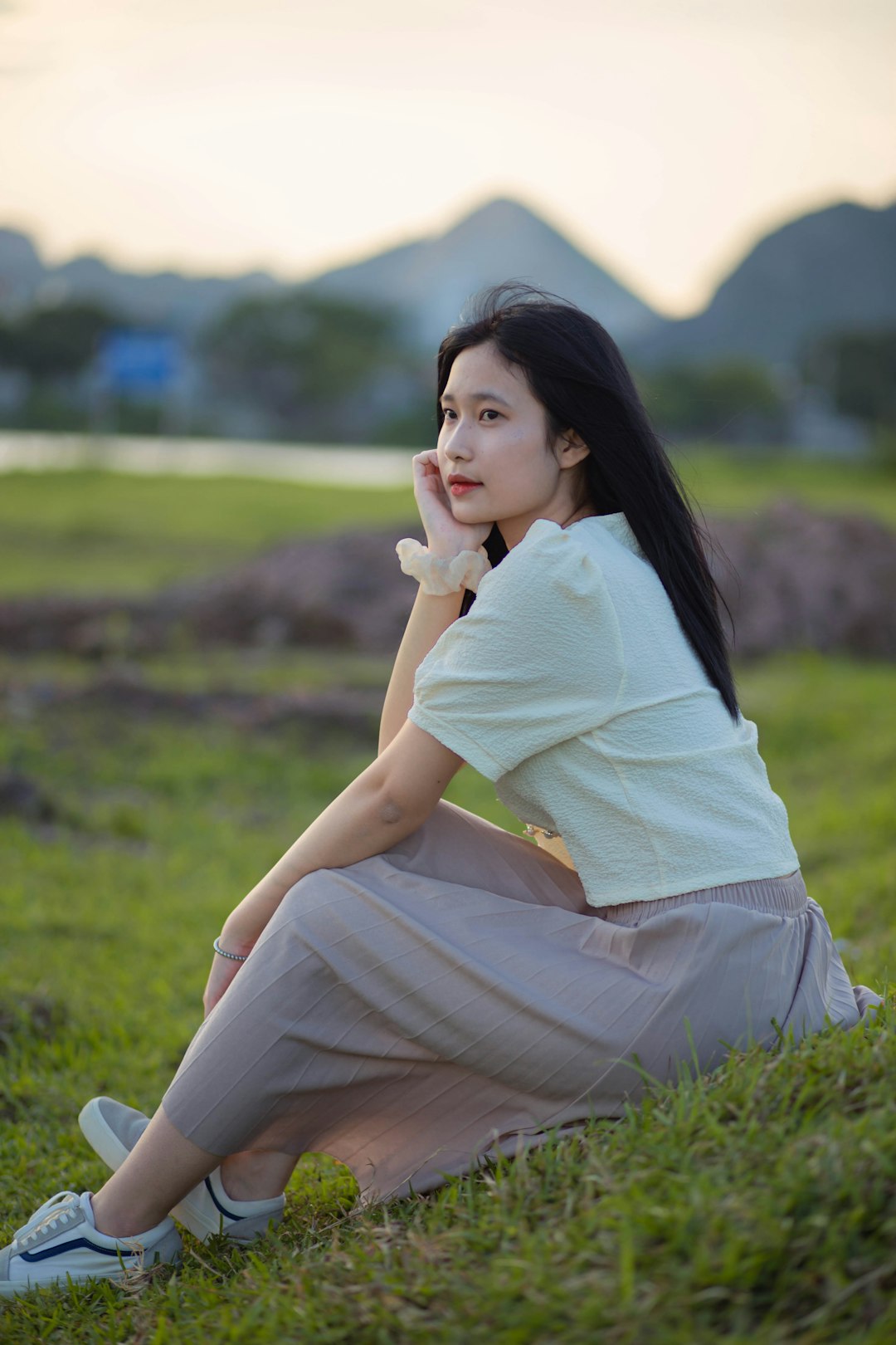 woman in white shirt and beige pants sitting on green grass field during daytime