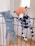 Two plush toys are hanging on a black metal railing. One toy resembles a blue elephant with a long nose, while the other is a spotted dog with an orange head. Both toys appear to be handmade and are positioned as if they are playfully hanging on the bars.