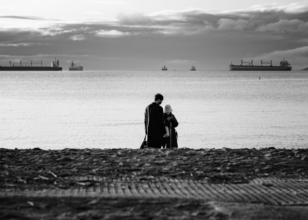 man and woman standing on the beach in grayscale photography