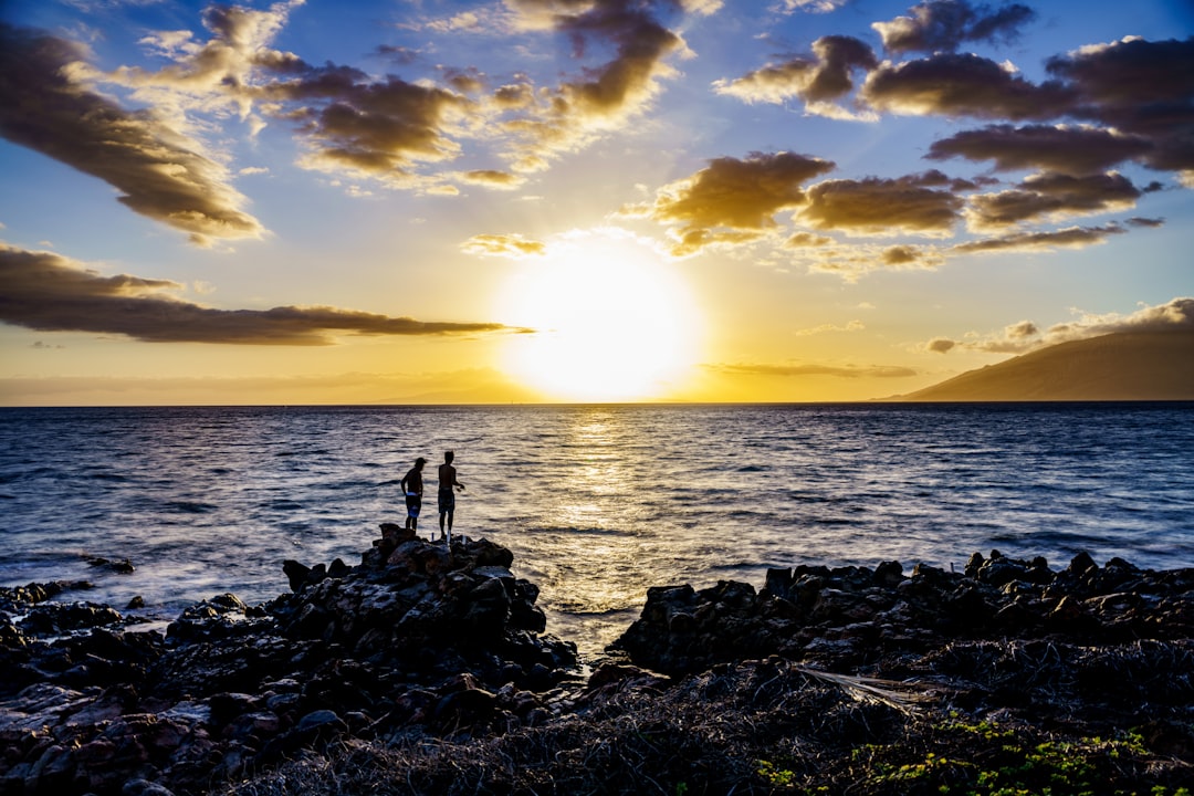 silhouette of person standing on rock near body of water during sunset