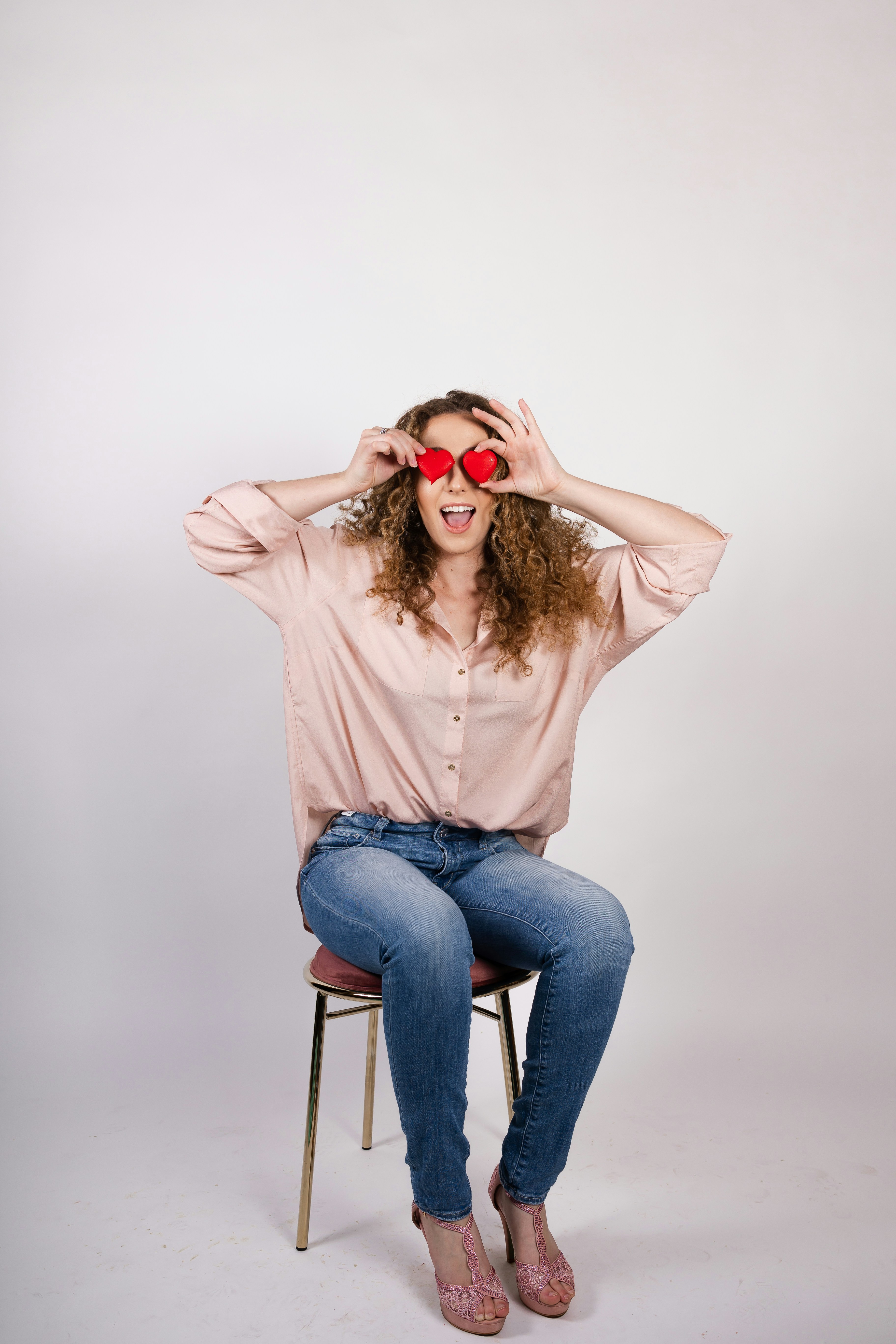 Woman holds hearts over her eyes, looking surprised.