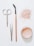 A flat lay arrangement of beauty tools and products on a white surface, including a pair of scissors, tweezers, a mascara wand with a wooden handle, a scattered amount of loose pink powder, and an open container filled with similar pink powder.