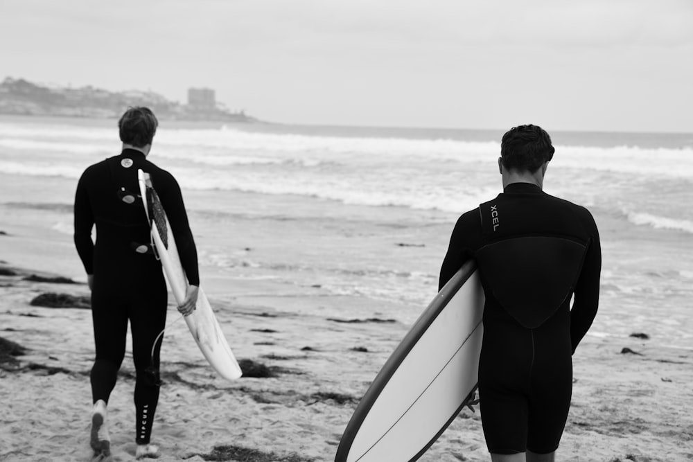 man in black jacket holding white surfboard walking on beach