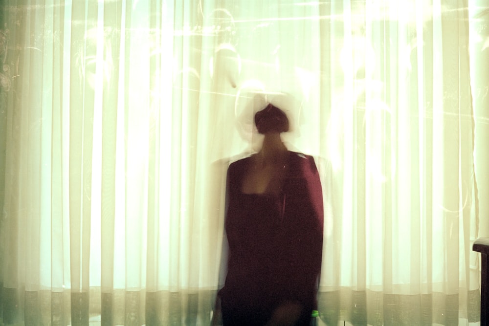 Mujer en camiseta sin mangas negra de pie cerca de la cortina blanca de la ventana