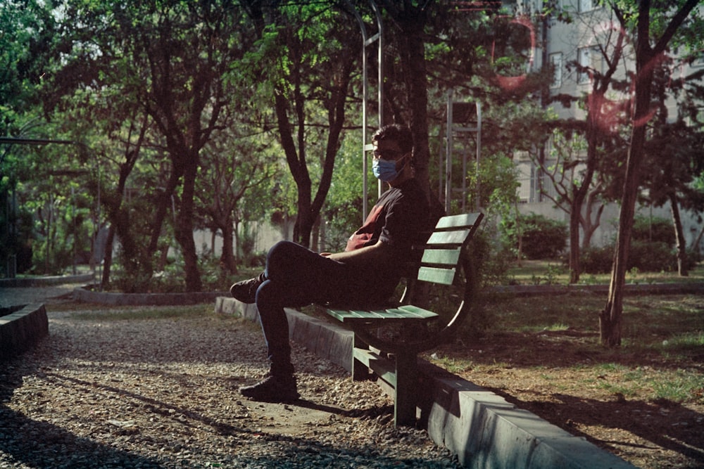 man in black jacket sitting on brown wooden bench