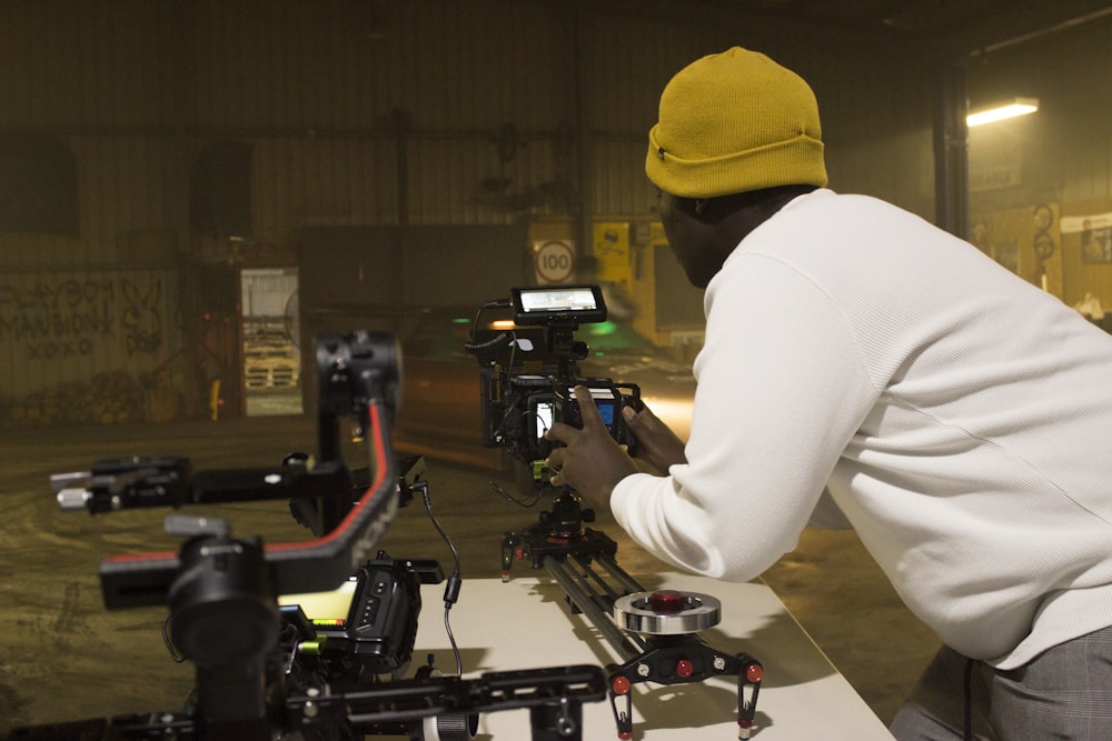 persona in berretto a maglia gialla e camicia bianca a maniche lunghe che tiene una videocamera nera