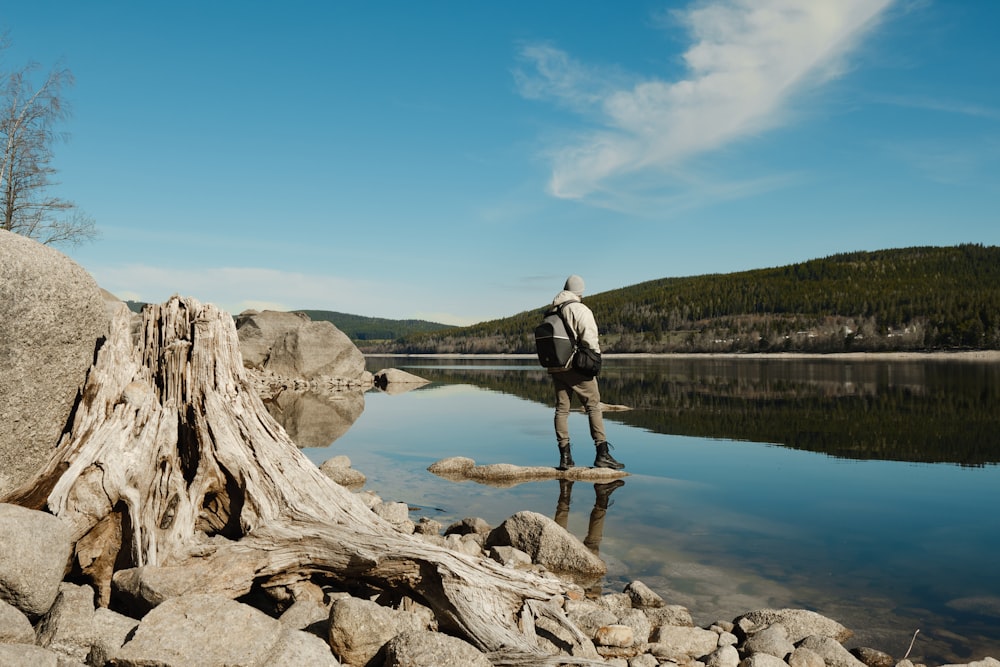 man in white shirt and black pants standing on rock near body of water during daytime