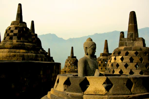 A stone Buddha statue among bell-shaped stupas at Borobudur temple in Indonesia