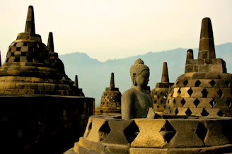 A stone Buddha statue among bell-shaped stupas at Borobudur temple in Indonesia