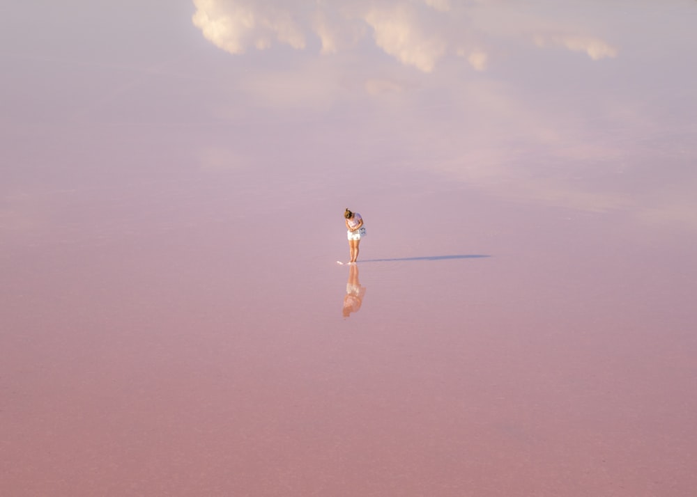 Mujer en vestido blanco de pie sobre arena marrón bajo cielo azul durante el día