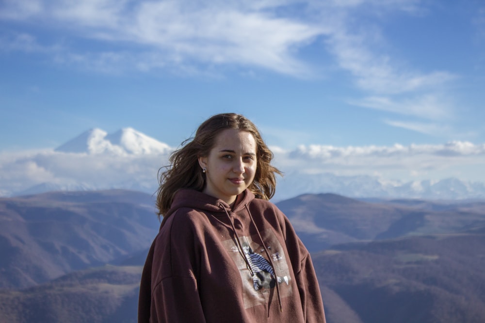 mujer con sudadera con capucha roja de pie en la cima de la montaña durante el día