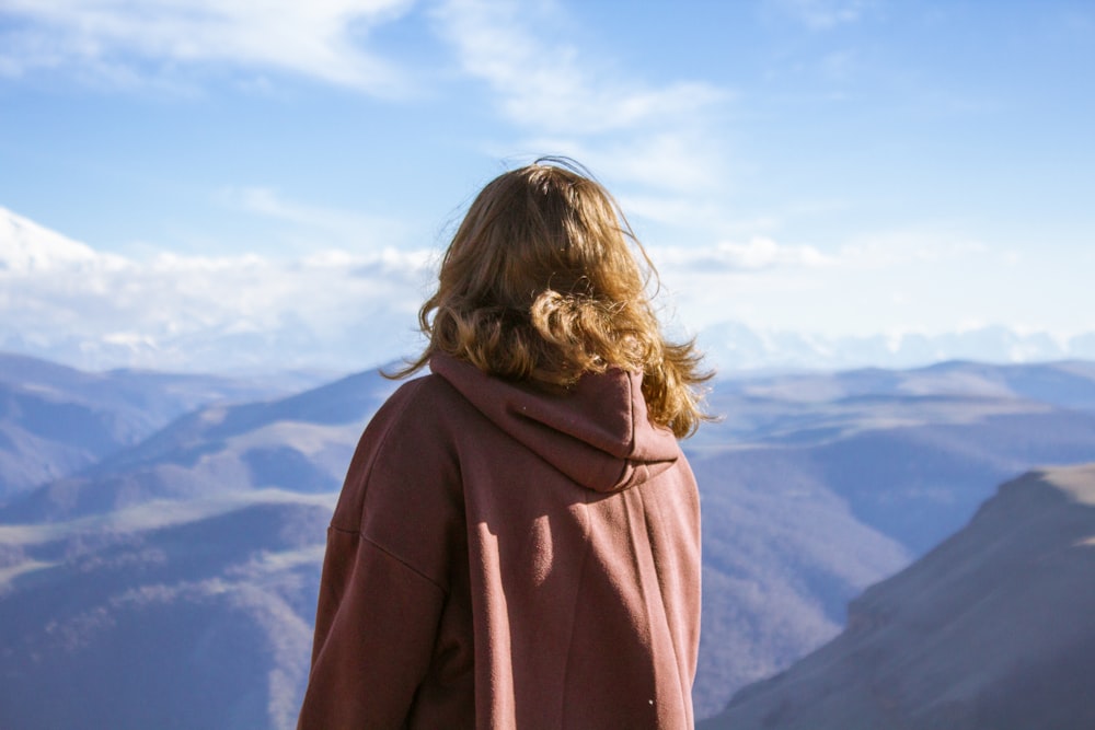 Donna in felpa con cappuccio marrone in piedi sulla cima della montagna durante il giorno