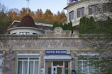 A historic building with a sign in Russian, indicating it is a post office. The architecture features a rounded structure with traditional design elements. Surrounding the building are trees and vegetation, and there is a visible sign with the name 'Post of Russia' near the entrance.