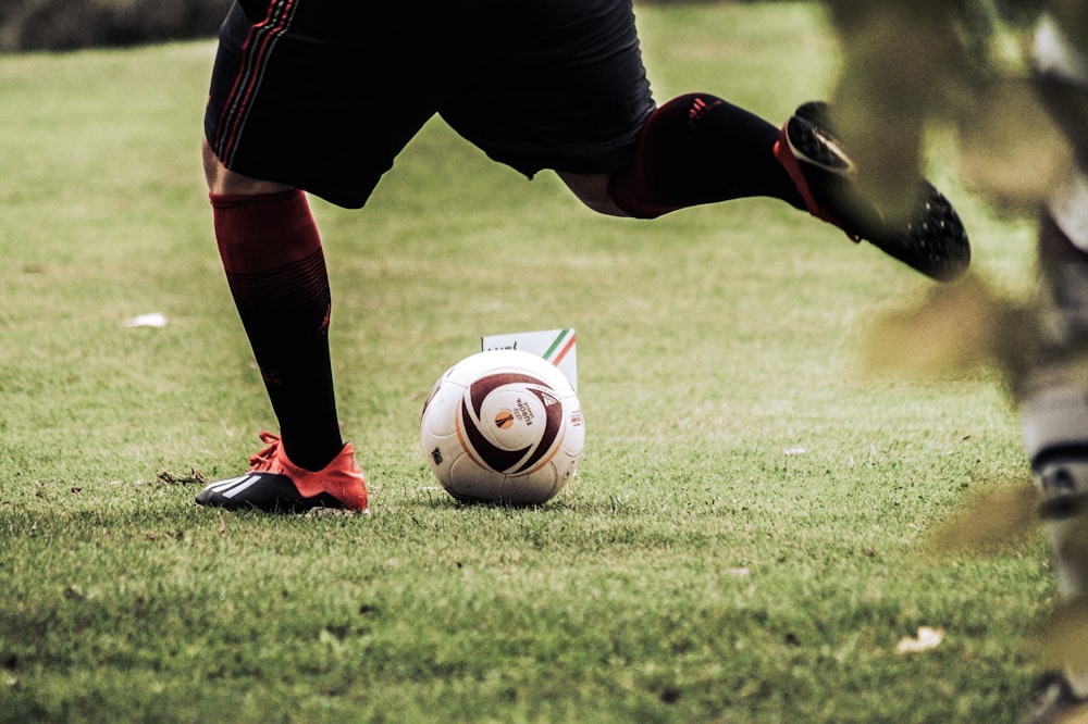 person in black shorts and white nike soccer ball on green grass field during daytime