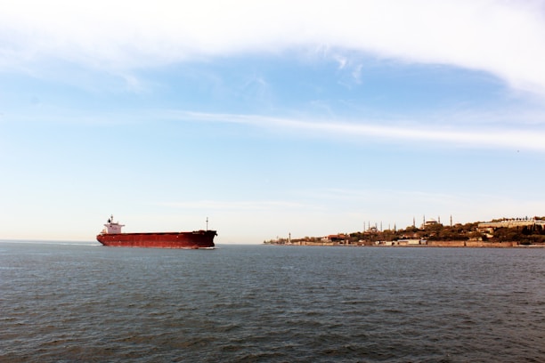 A cargo ship loaded with oil barrels sailing from Dubai port under a clear sky.