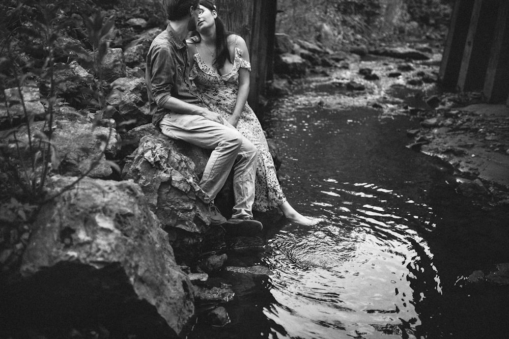 grayscale photo of woman in dress sitting on rock in water