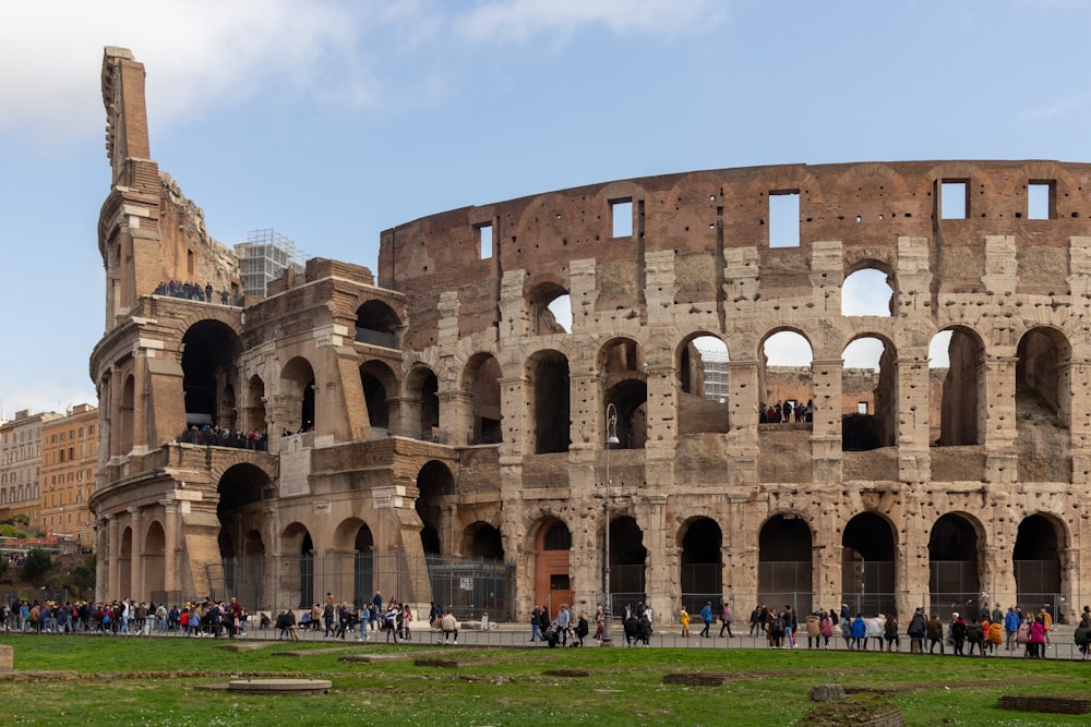 Persone che camminano sul campo di erba verde vicino all'edificio in cemento marrone durante il giorno