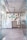 A modern entrance to a co-working space featuring glass doors with diagonal patterns, leading into a room with a decorative wall. The wall includes various objects and an eye-catching logo for the space. The floors are wooden and there are visible industrial-style ceiling fixtures.