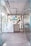 A modern entrance to a co-working space featuring glass doors with diagonal patterns, leading into a room with a decorative wall. The wall includes various objects and an eye-catching logo for the space. The floors are wooden and there are visible industrial-style ceiling fixtures.
