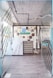 A modern entrance to a co-working space featuring glass doors with diagonal patterns, leading into a room with a decorative wall. The wall includes various objects and an eye-catching logo for the space. The floors are wooden and there are visible industrial-style ceiling fixtures.